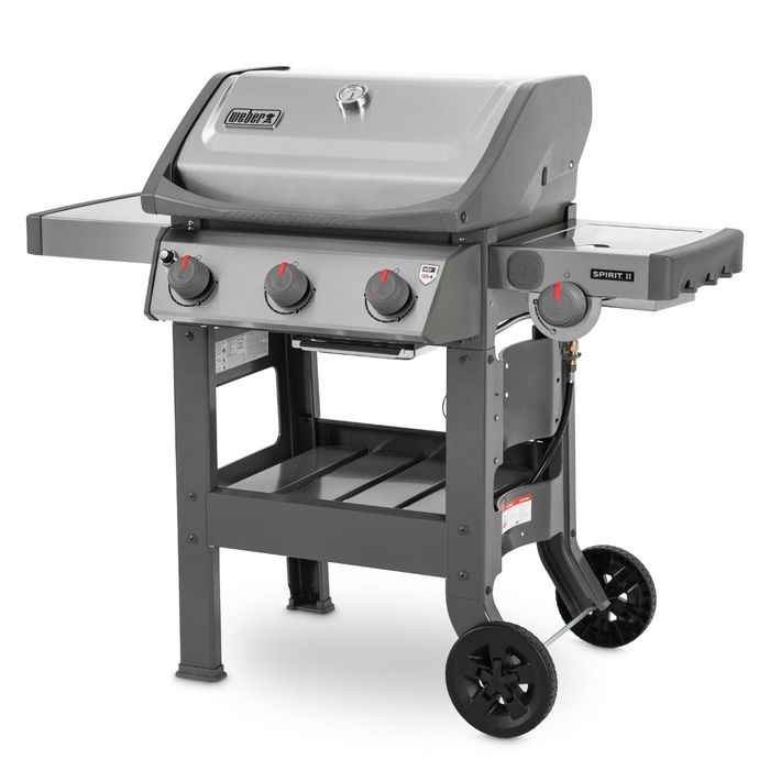 Grill gazowy Weber Spirit II S-320 GBS ustawiony bokiem, z szarą pokrywą i termometrem regulującym temperaturę, po bokach grilla widoczne są dwie szare półki, z przodu cztery pokrętła z czerwonym wskaźnikiem.