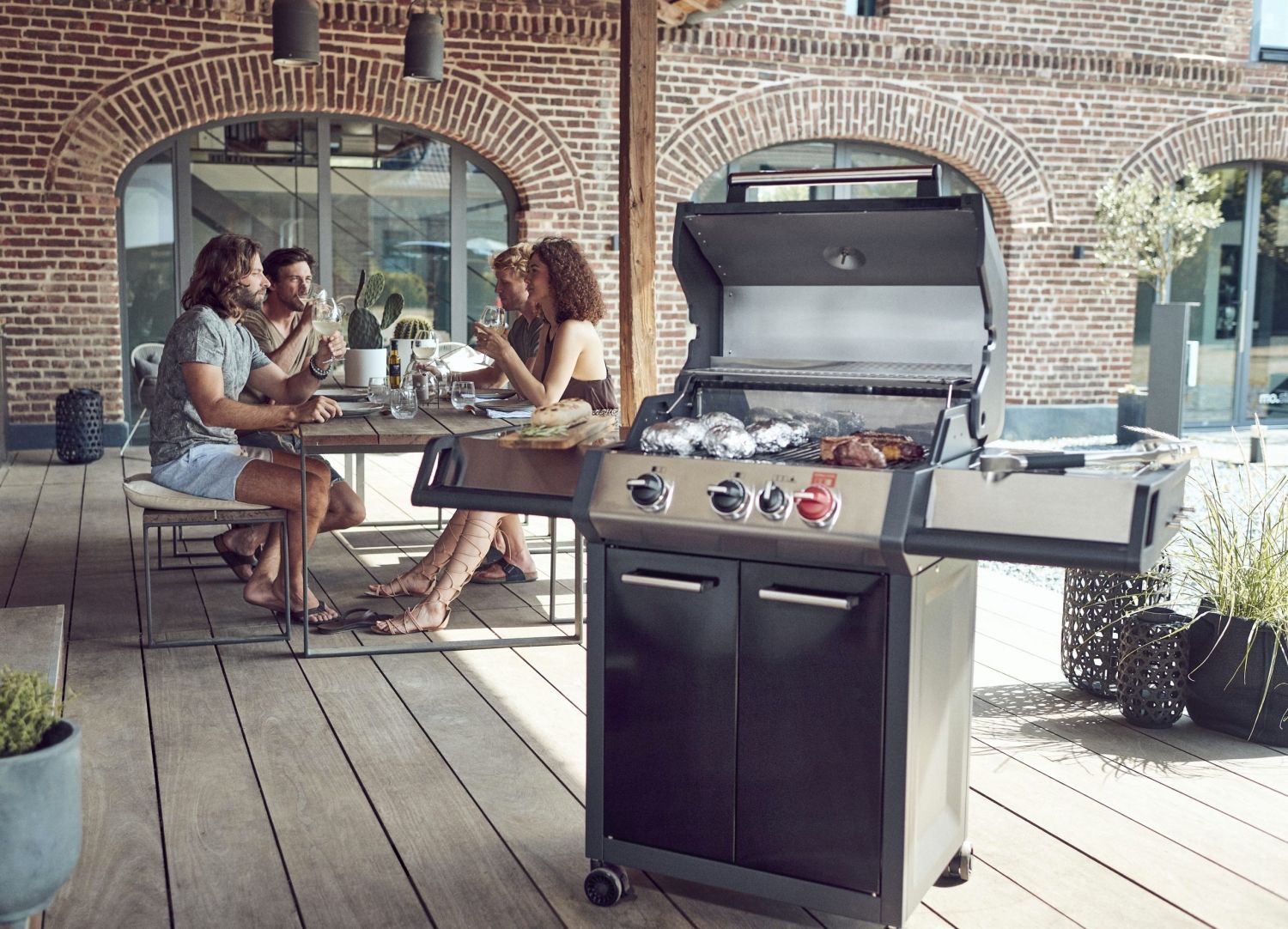 Grill gazowy Enders Monroe Pro 3K turbo, w tle ludzie jedzący posiłek.