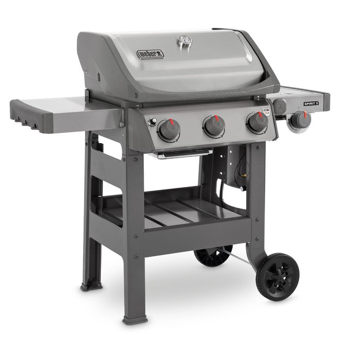 Grill gazowy Weber Spirit II S-320 GBS ustawiony bokiem, z szarą pokrywą i termometrem regulującym temperaturę, po bokach grilla widoczne są dwie szare półki, z przodu cztery pokrętła z czerwonym wskaźnikiem.