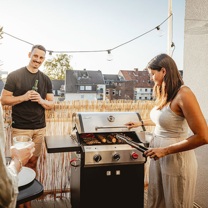 Para przygotowująca posiłek na grillu Enders Chicago Next 3 R Turbo w słoneczny dzień na nowoczesnym tarasie.