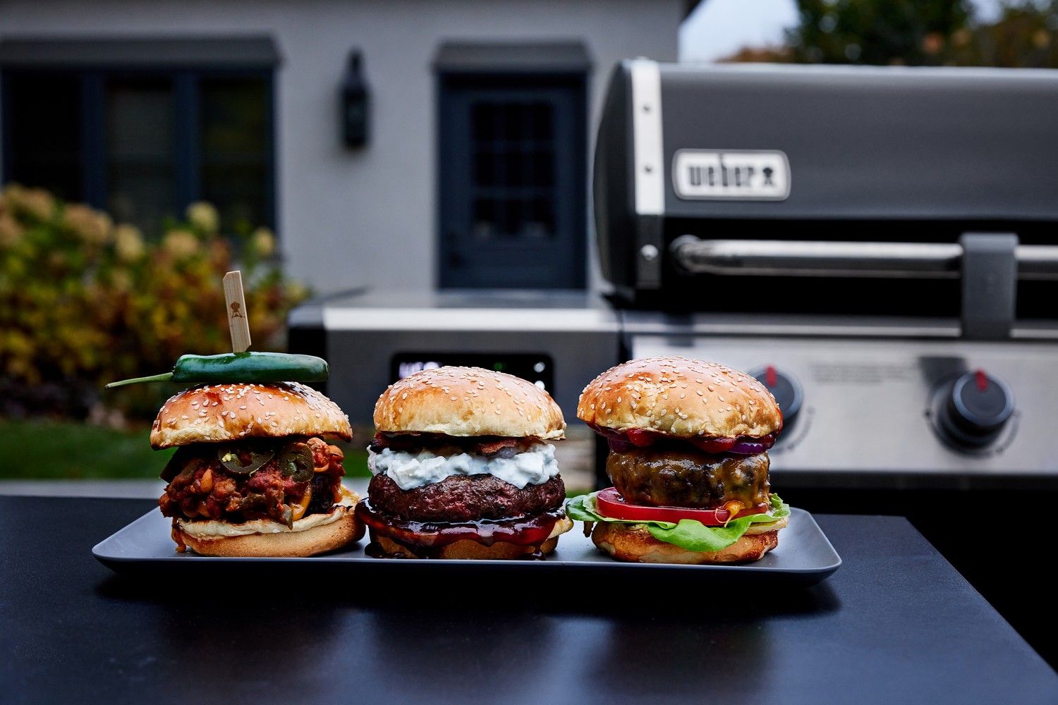 Trzy burgery i grill gazowy Weber w tle